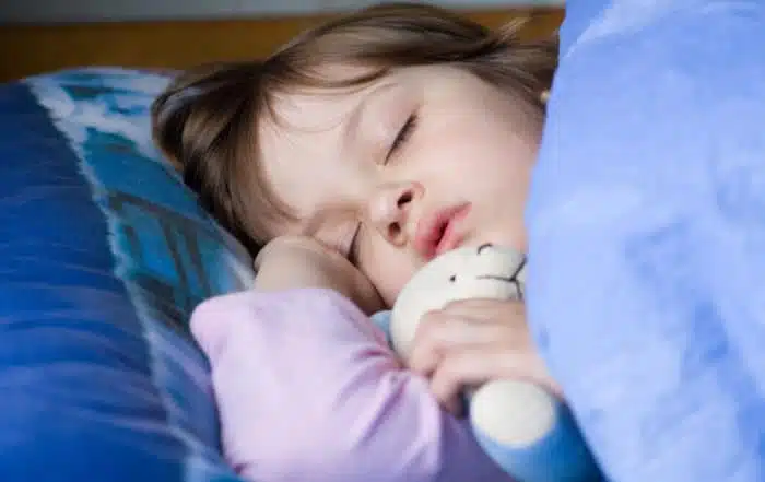 kid is sleeping on the bed with tedy bear